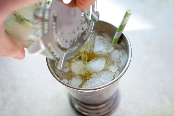pouring a mint julep cocktail into a glass
