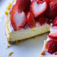 Instant Pot Cheesecake with piece cut out and strawberries on top on white plate