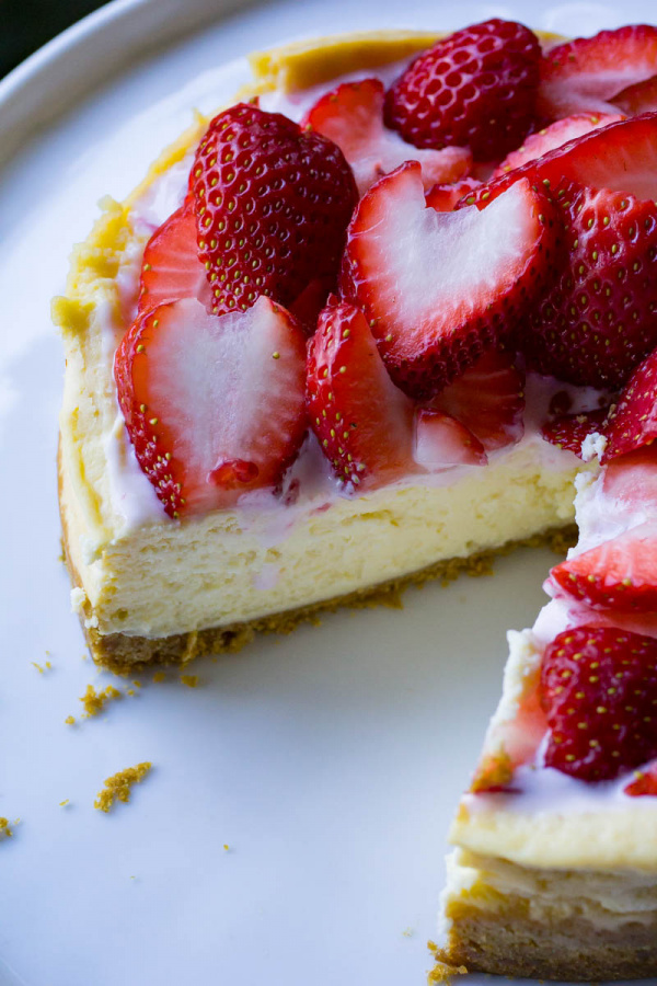 Instant Pot Cheesecake with piece cut out and strawberries on top on white plate