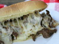 cajun cheesesteak sandwich on a white plate set on a white and red checked napkin