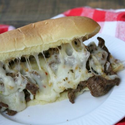 cajun cheesesteak sandwich on a white plate set on a white and red checked napkin