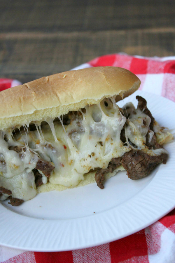 Cajun Cheesesteak Sandwiches from RecipeGirl.com #cajun #cheesesteak #sandwich #cheese #recipe #easy #dinner #recipe #RecipeGirl Cajun Cheesesteak Sandwich on a white plate with a red/white checked napkin underneath