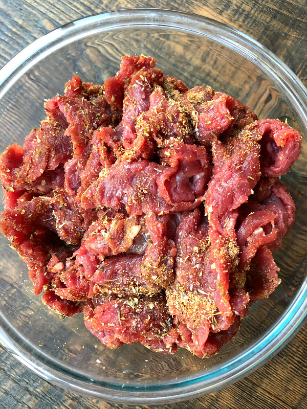 Flank Steak seasoned with Cajun seasoning in a glass bowl on a wood surface