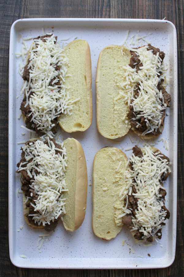 Open faced cajun cheesesteak sandwiches on a white baking sheet ready for the oven