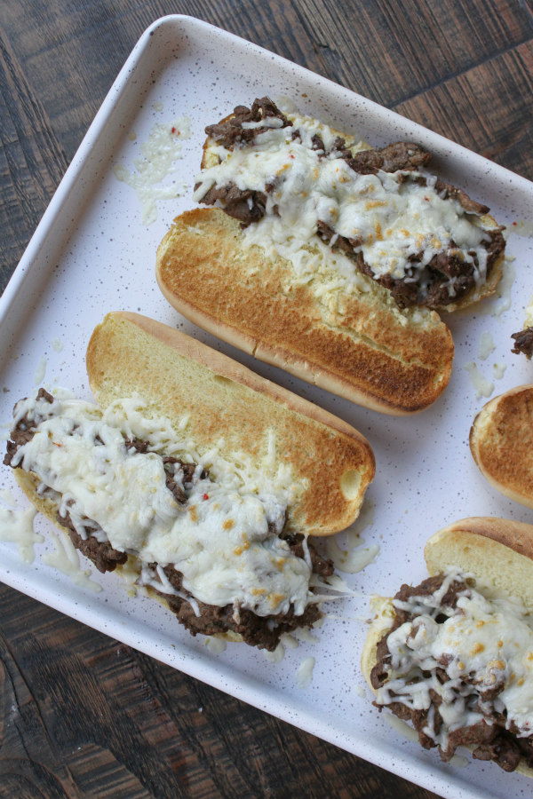 Cajun Cheesesteak Sandwiches from RecipeGirl.com #cajun #cheesesteak #sandwich #cheese #recipe #easy #dinner #recipe #RecipeGirl open faced Cajun Cheesesteak Sandwiches out of the oven on a white baking sheet