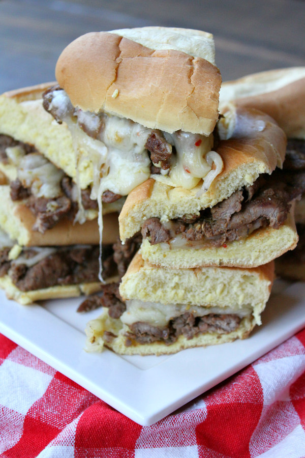 slices of Cajun Cheesesteak Sandwiches stacked on a white plate on top of a white/red checked napkin