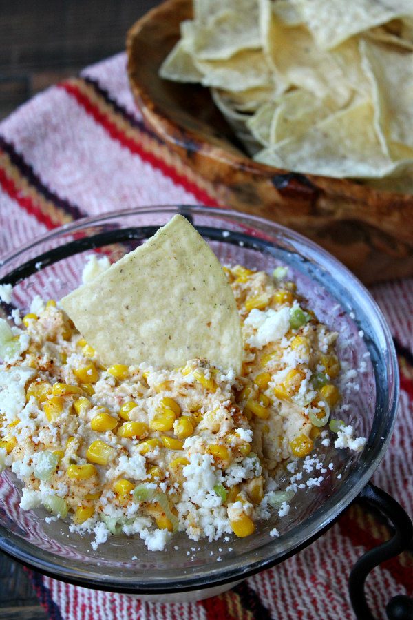 Mexican Street Corn Dip in a glass bowl served with chips set on a colorful Mexican blanket