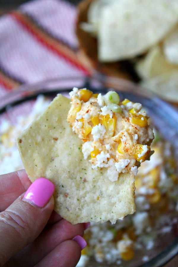 Mexican Street Corn Dip on a chip - fingers holding have pink fingernails