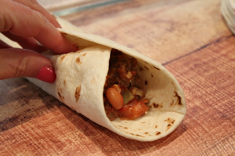 wrapping a tortilla around beef and bean filling