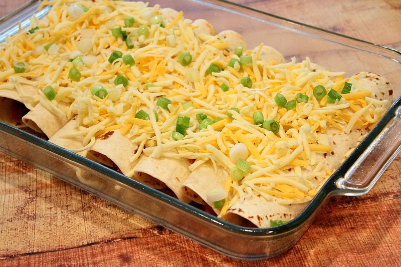 beef burrito casserole ready to go in the oven with shredded cheese and green onions on top