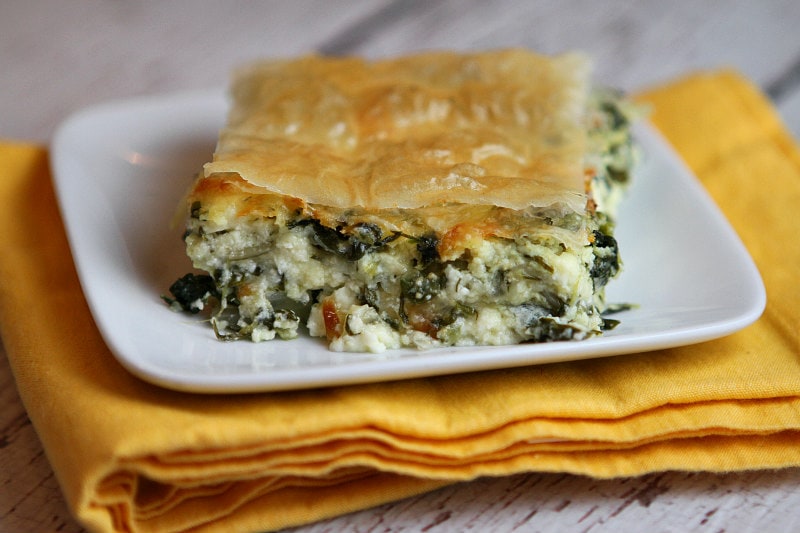 Slice of Greek Spinach Pie on white plate set on yellow napkin