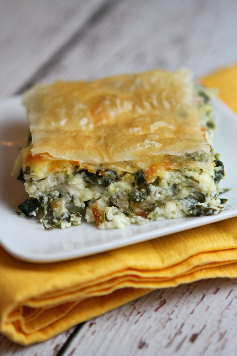 Slice of Greek Spinach Pie on white plate set on yellow napkin