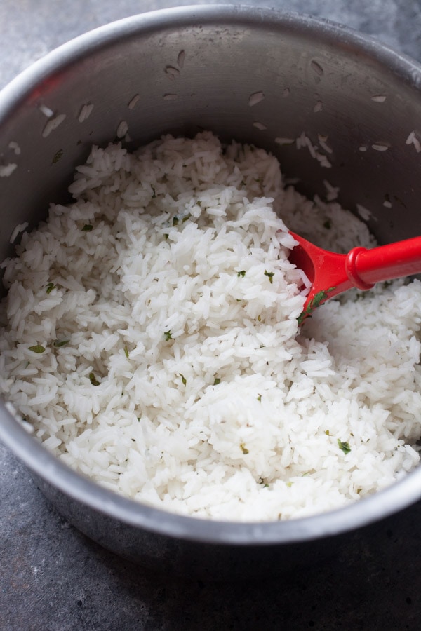 Cilantro Rice in a silver saucepan with a red serving spoon