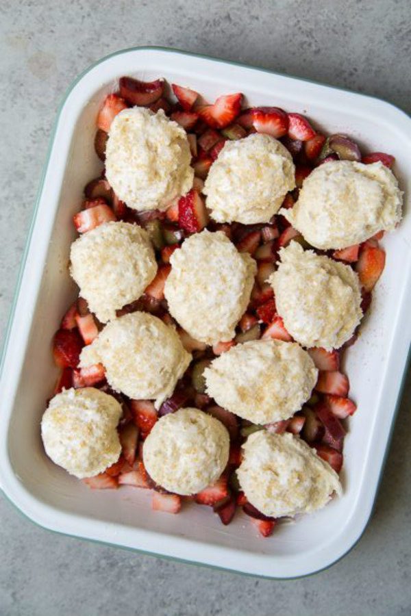 Biscuits on top of Strawberry Rhubarb Cobbler in a white casserole dish ready for the oven
