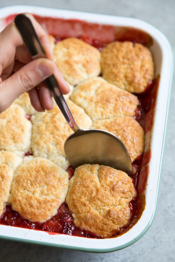 Spooning out Strawberry Rhubarb Cobbler out of the white casserole dish
