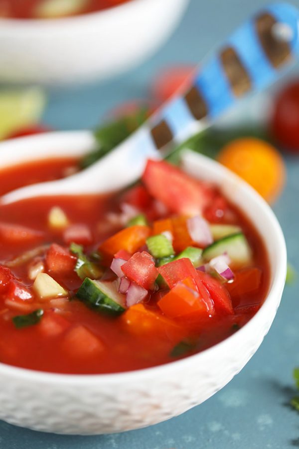 Gazpacho in a white bowl garnished with tomato and cucumber and a spoon