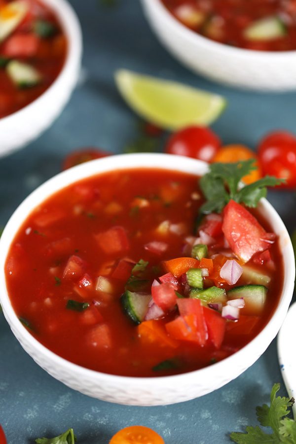 Gazpacho in a white bowl garnished with tomato and cilantro and lime