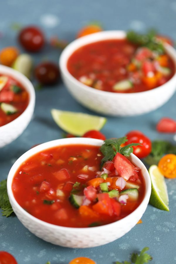 three white Bowls of Gazpacho garnished with cilantro, tomato and lime