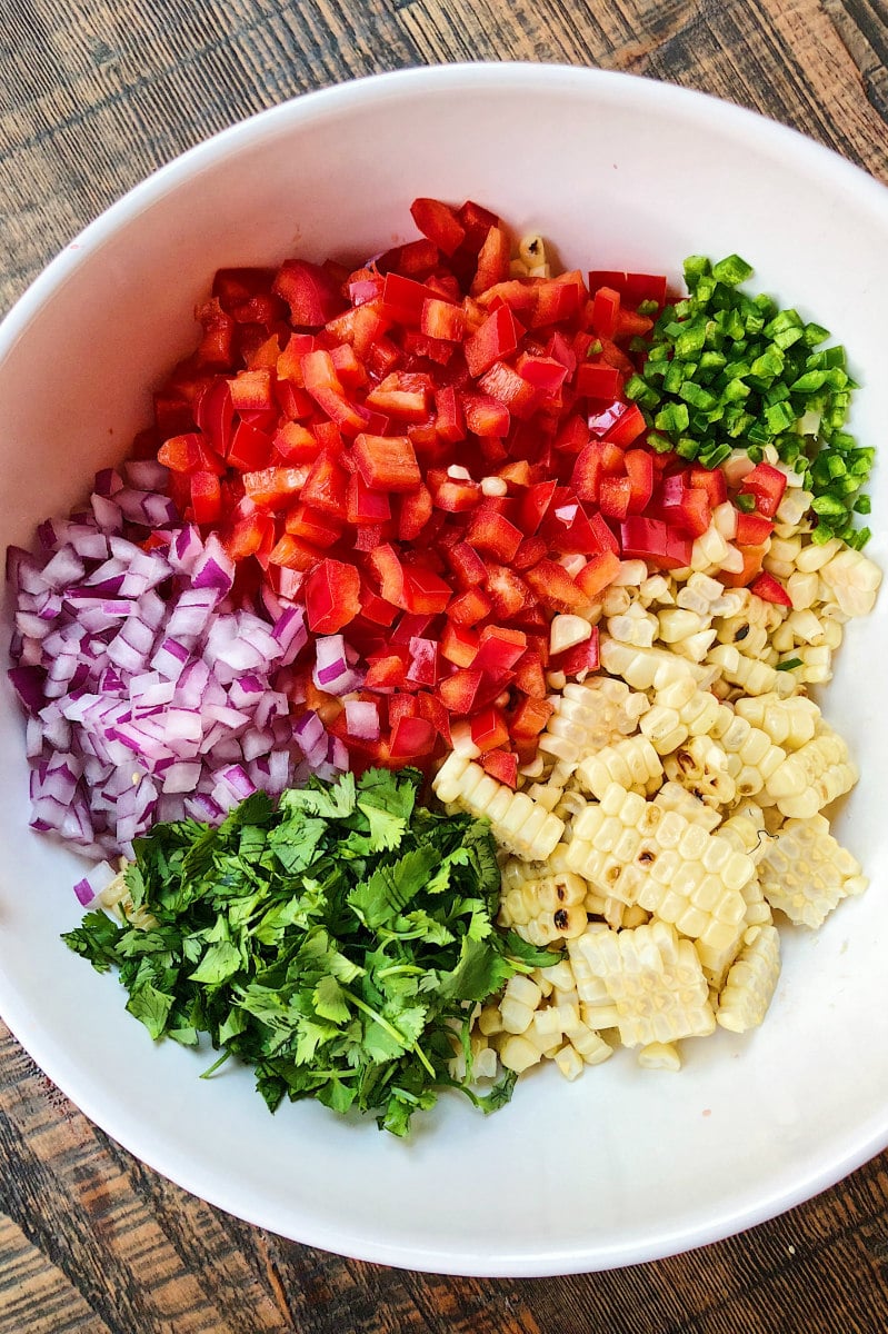 ingredients for Grilled Corn Salad in a white bowl set on a wooden surface