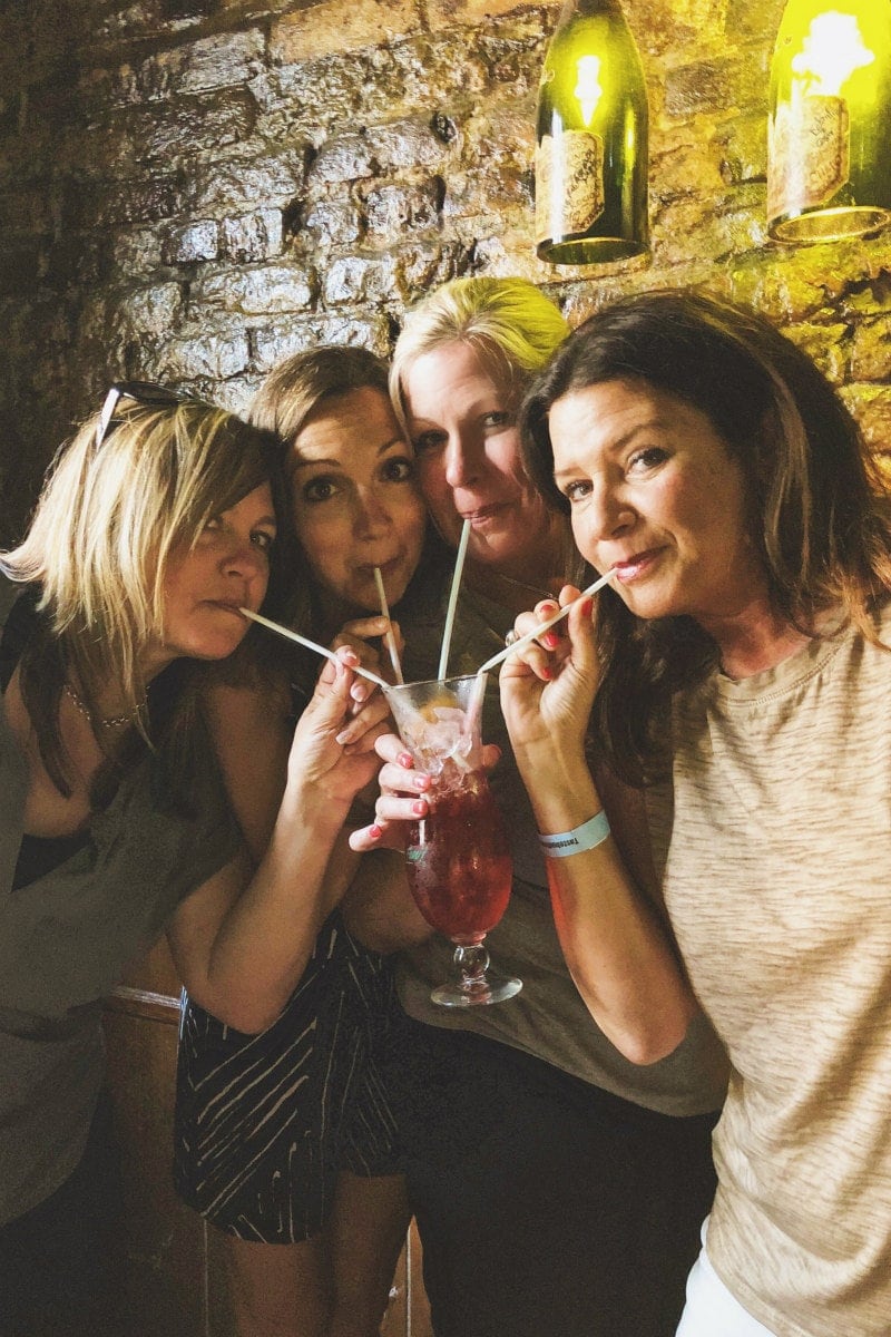 four girls sharing a hurricane cocktail with straws