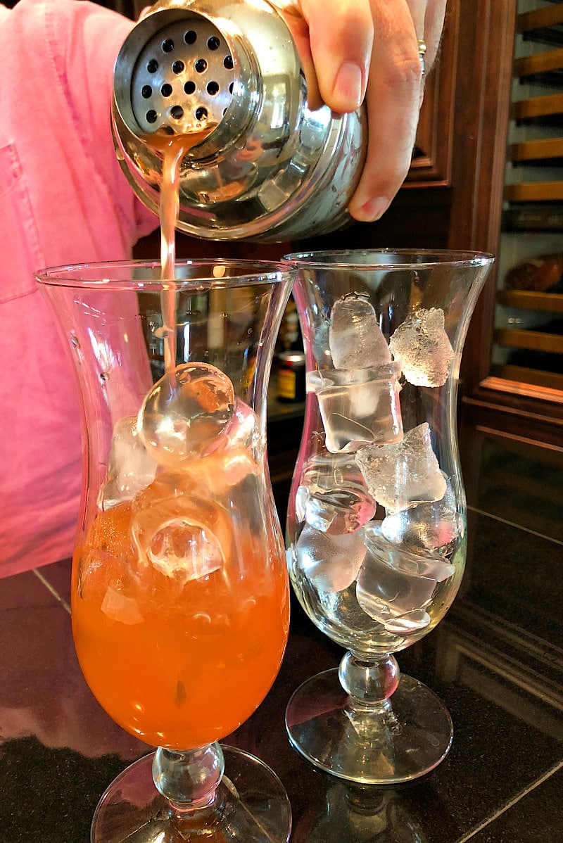 man in a pink shirt pouring hurricane cocktails into hurricane glasses