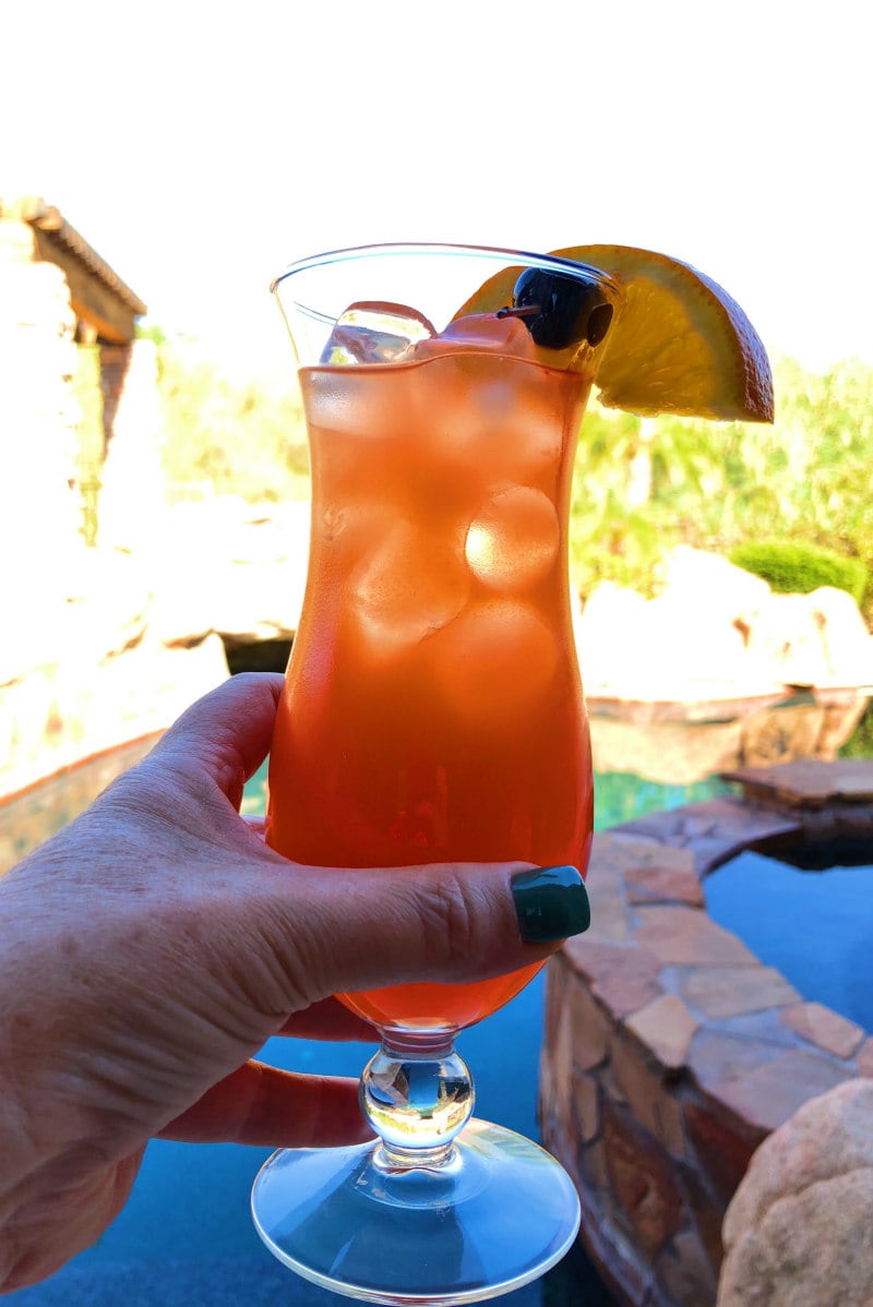 hand holding a hurricane cocktail with a backyard in the background