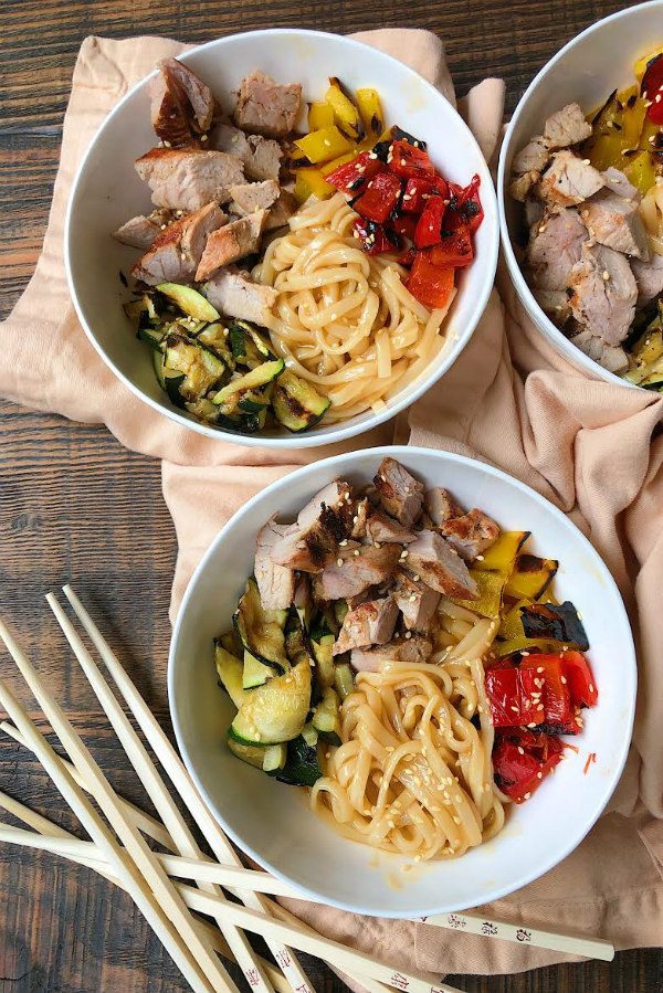 Two Grilled Pork and Vegetable Teriyaki Noodle Bowls in white bowls. Chopsticks on the side and a peek at a third bowl in the background