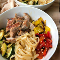 grilled pork and vegetable teriyaki noodle bowl in a white bowl. a peek at a 2nd noodle bowl in the background