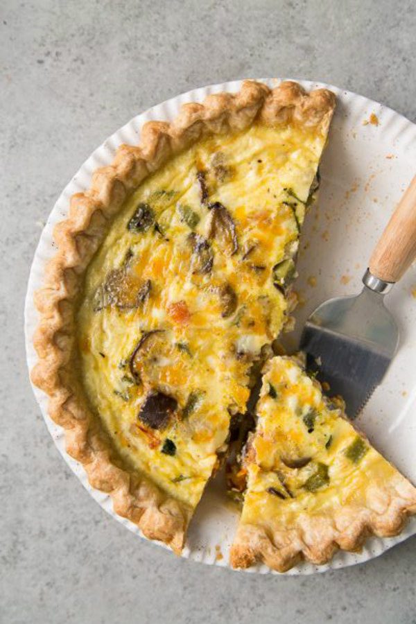 Summer Vegetable Quiche in a white pie plate with a couple of pieces cut out and a pie server on the plate