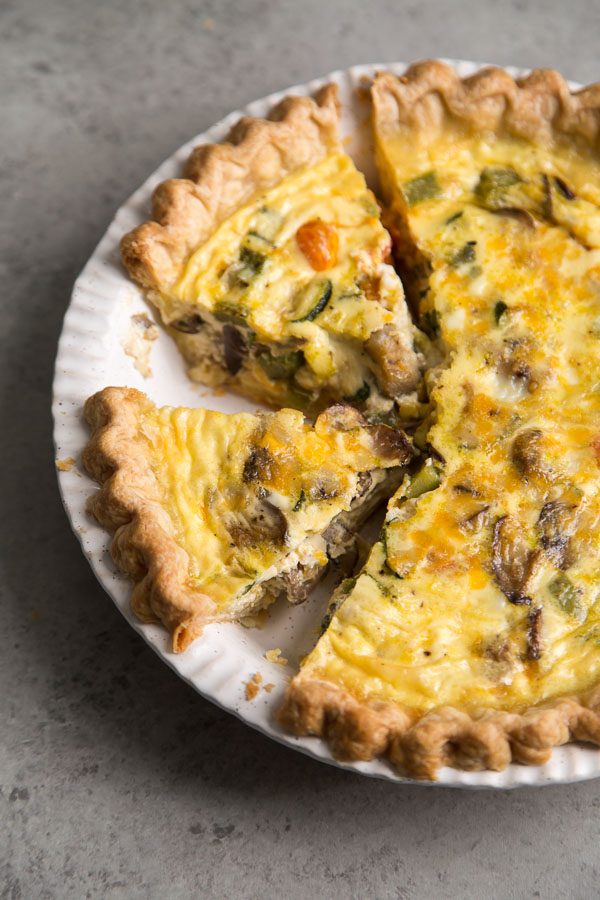 Summer Vegetable Quiche in a white pie plate with a couple of pieces cut out