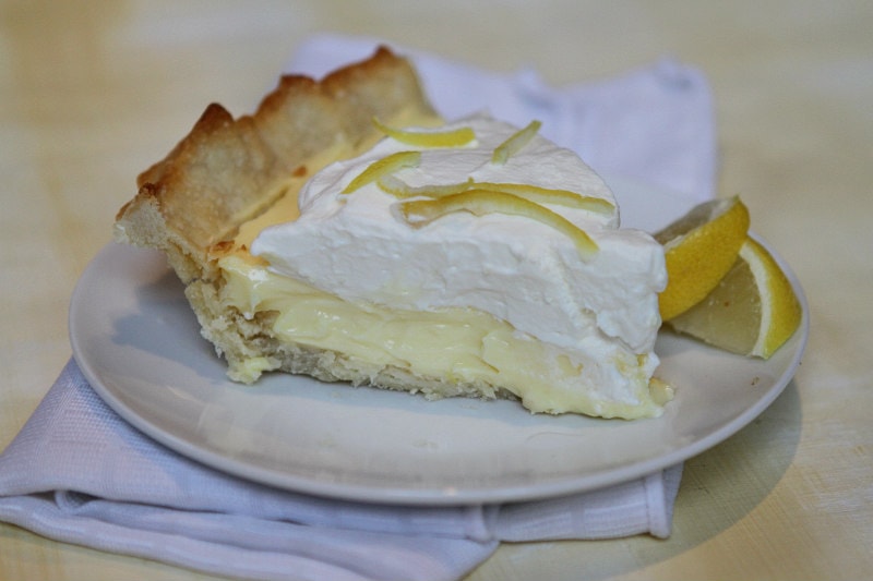slice of Lemon Sour Cream Pie on a white plate, garnished with lemon slices. Setting on a white napkin.