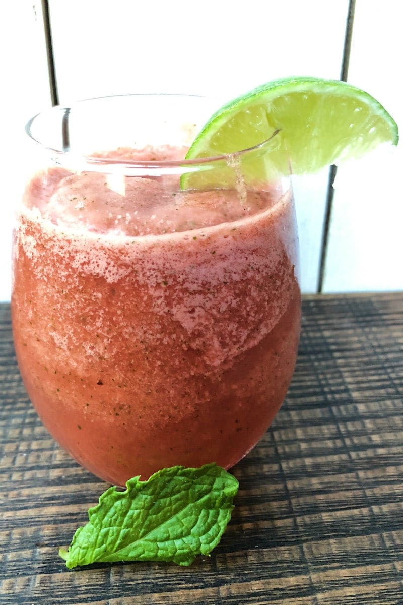 slushie watermelon mojitos in a glass garnished with a lime wedge and a mint leaf in front of the glass