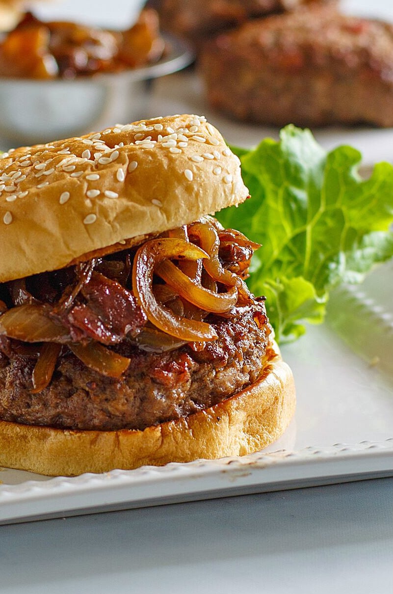 Bacon Burgers with Balsamic Caramelized Onions recipe from RecipeGirl.com #bacon #burgers #balsamic #caramelized #onions #recipe #RecipeGirl Bacon Burger with Balsamic Caramelized Onions on a white platter with a lettuce leaf