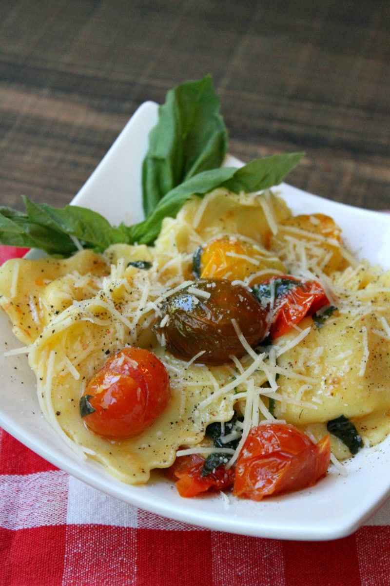 brown butter ravioli with tomatoes on a white plate set on a red/white checked napkin