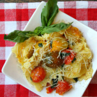 overhead shot of brown butter ravioli with tomatoes on a white plate set on a red/white checked napkin