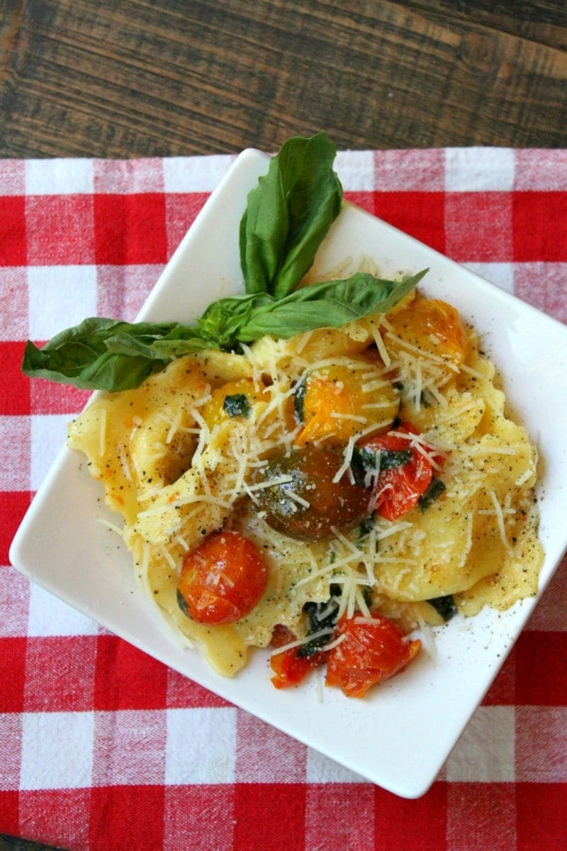 overhead shot of brown butter ravioli with tomatoes on a white plate set on a red/white checked napkin