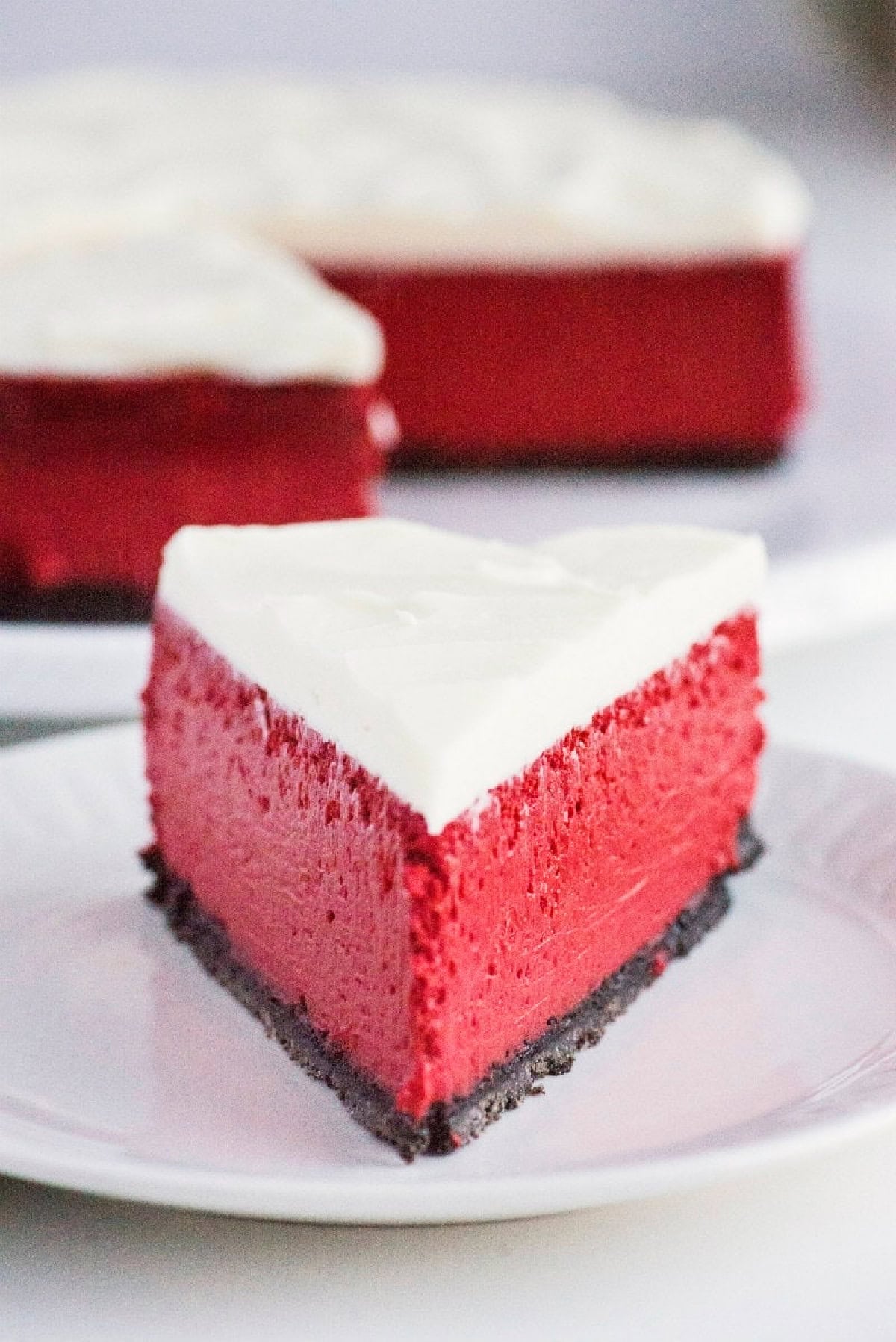 This gorgeous Red Velvet Cheesecake has a creamy red velvet filling, chocolate Oreo crust and rich cream cheese frosting. It's an impressive make-ahead dessert for Christmas, Valentine's Day, holidays and special occasions. slice of red velvet cheesecake on plate