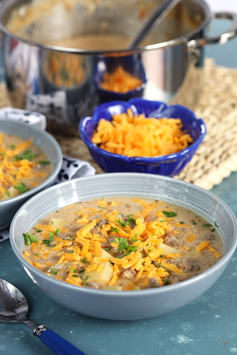 Creamy cheeseburger soup in a gray bowl with grated cheddar on top on a blue background.