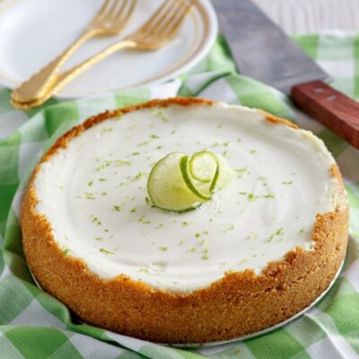 key lime cheesecake set on green/white checked napkin with forks, serving spatula and plates in the background