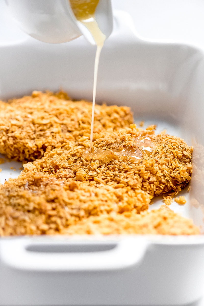 Making Baked Cornflake Chicken- chicken dipped and placed in white casserole dish with melted butter being poured on top