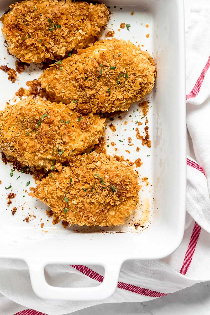 Baked Cornflake Chicken in a white casserole dish set on a white and red striped towel