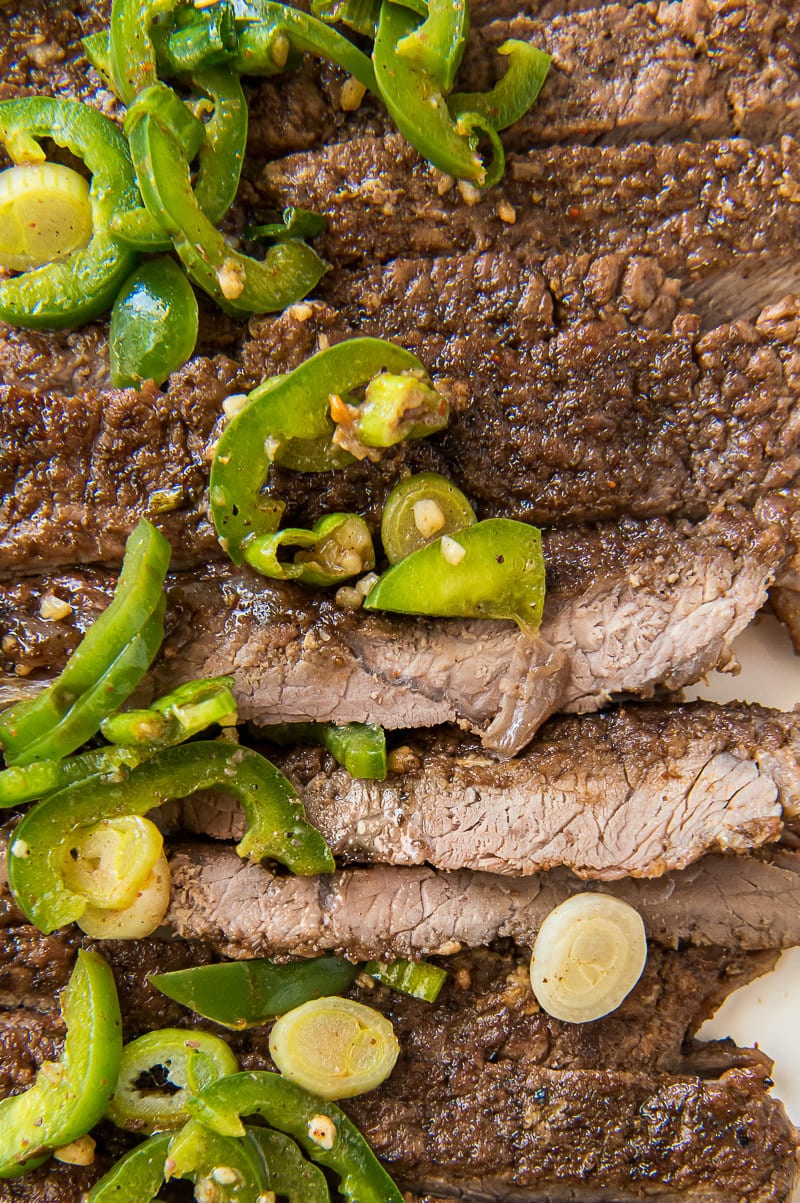 sliced carne asada close up topped with sliced jalapenos