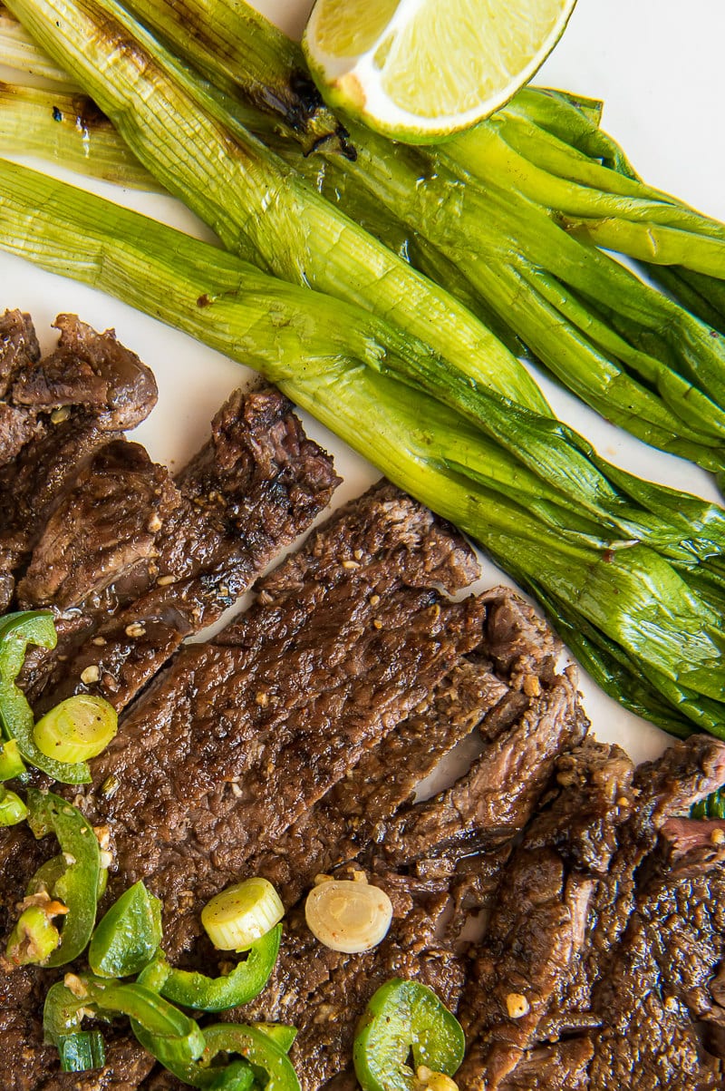 Easy Grilled Carne Asada recipe from RecipeGirl.com #easy #homemade #mexican #authentic #grilled #carne #asada #carneasada #recipe #RecipeGirl sliced carne asada topped with sliced jalapeno with green onions and lime on the side