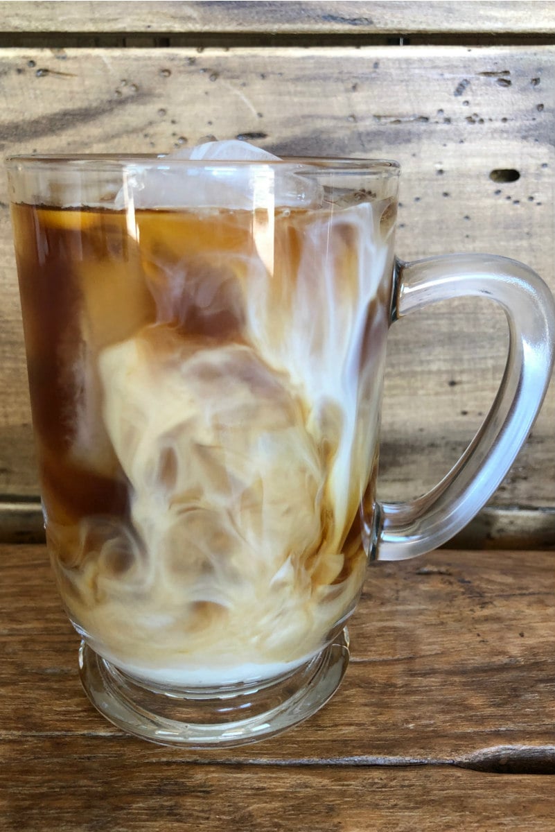 glass mug of cold brew coffee with cream swirling around in it