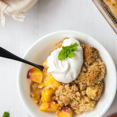 serving of peach cobbler french toast casserole in a white bowl garnished with whipped cream and fresh mint