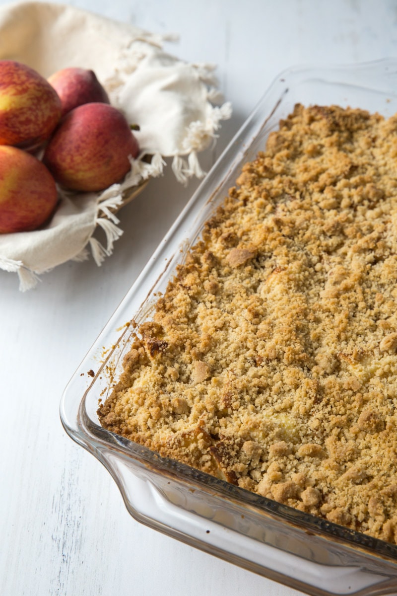 peach cobbler french toast casserole in a pyrex pan with a basket of fresh peaches in the background