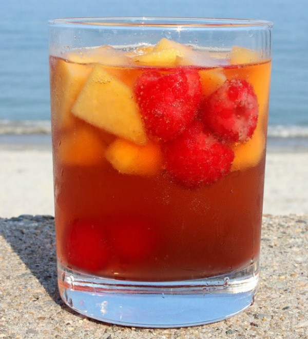 glass of carolina peach sangria sitting on a sea wall with the beach in the background