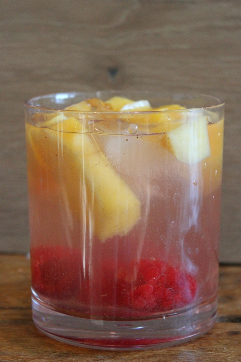 peach and raspberry sangria in a glass with a wood backdrop