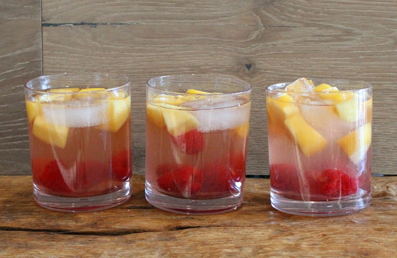 three glasses of peach and raspberry sangria with a wooden backdrop