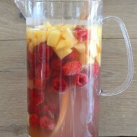 pitcher of peach and raspberry sangria with a wood backdrop
